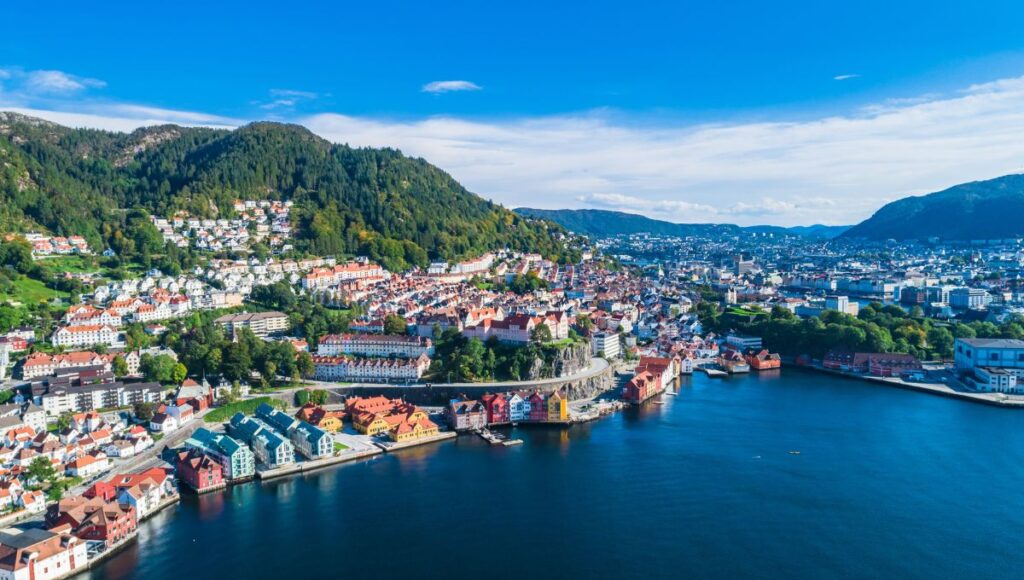 Aerial view of Bergen, Norway, with colourful waterfront buildings and surrounding mountains.
