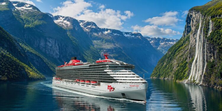 Virgin Voyages' Valiant Lady sailing through the Norwegian Fjords surrounded by mountains and waterfalls.