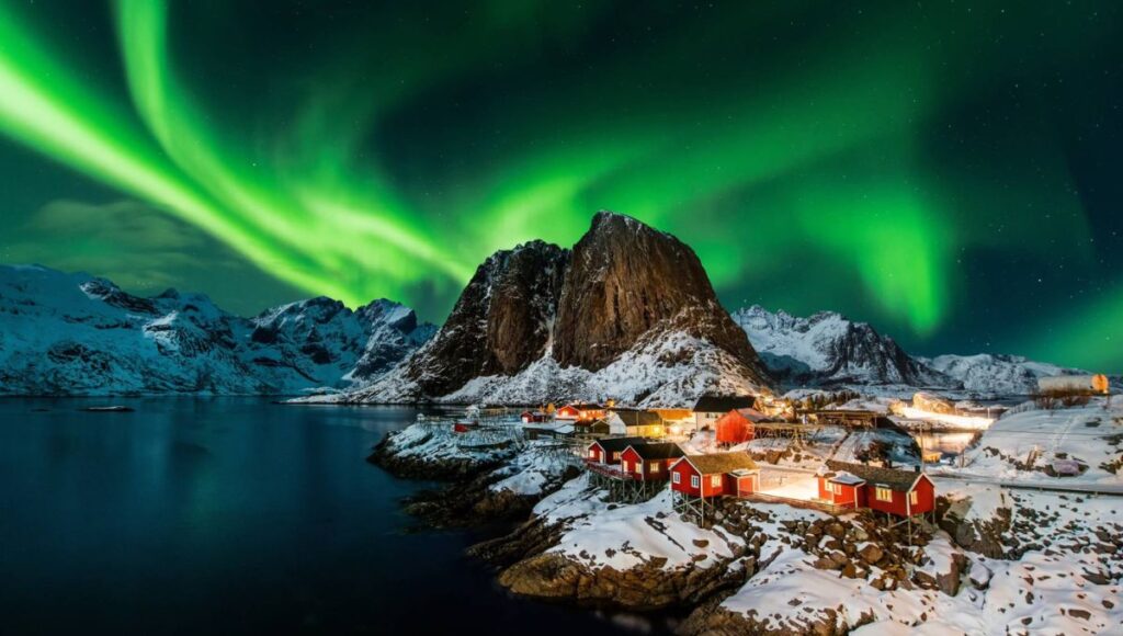 Northern Lights glowing above a snow-covered fishing village in Norway’s Lofoten Islands.
