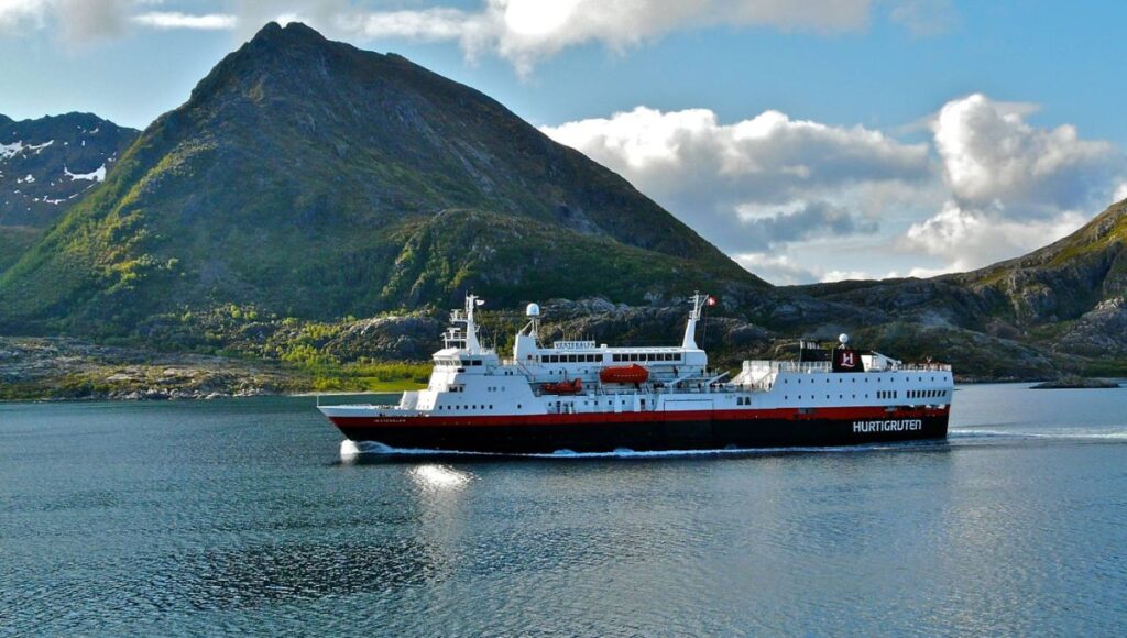 Hurtigruten coastal ship sailing past mountainous scenery along the Norwegian coast.