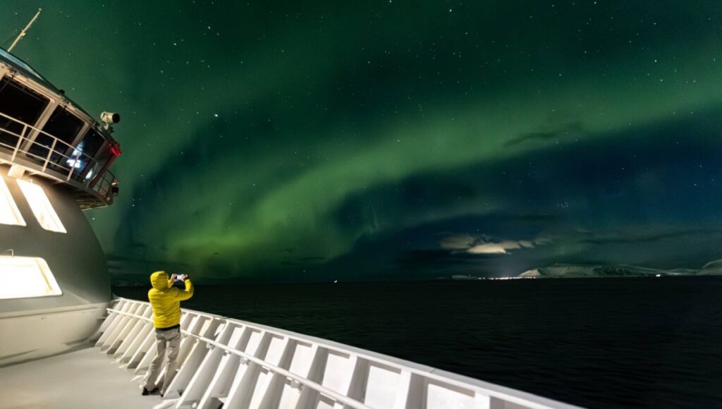 Guests watching the Northern Lights from the outdoor deck during a winter Norwegian coastal voyage.