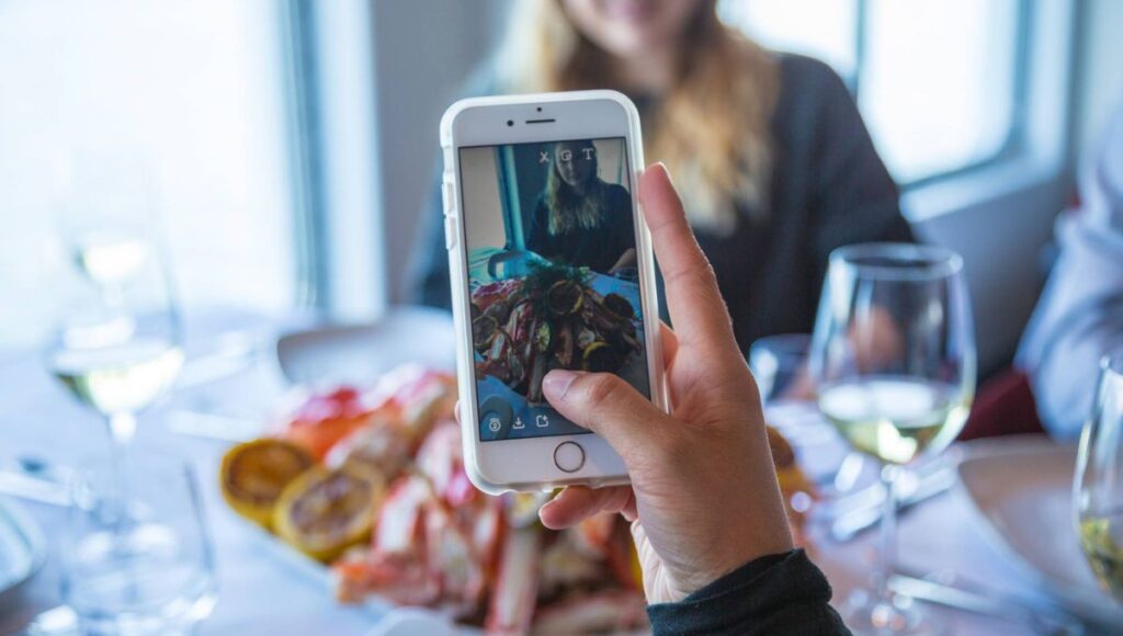 Cruise passenger photographing a seafood dish on their phone during a Norwegian coastal voyage.