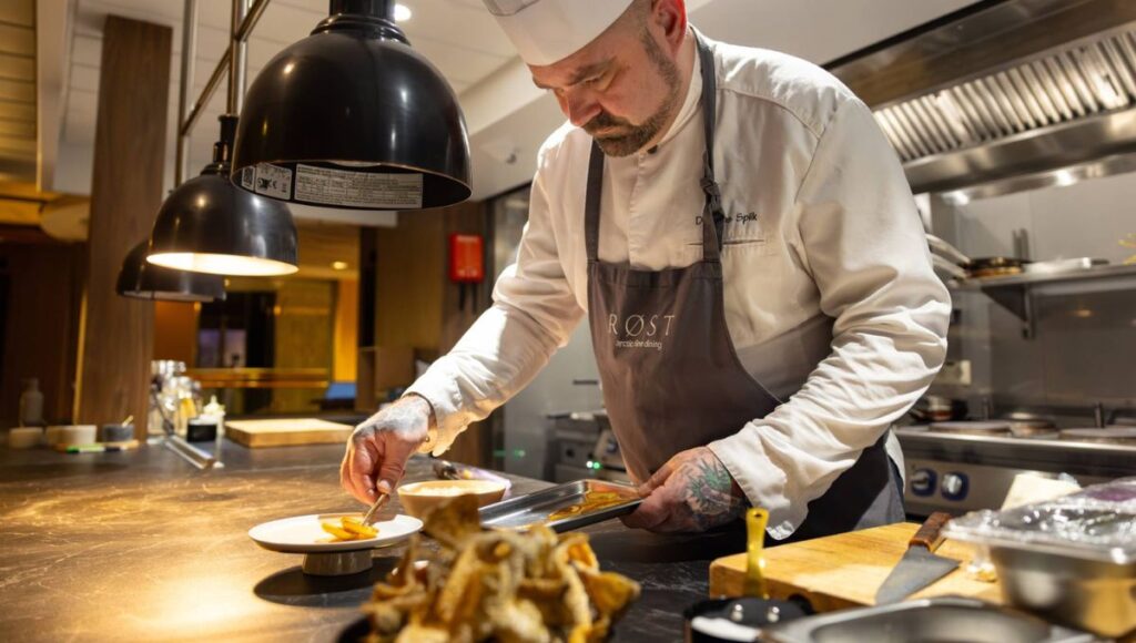 Chef preparing a freshly plated dish in the kitchen aboard a Norwegian coastal cruise ship.