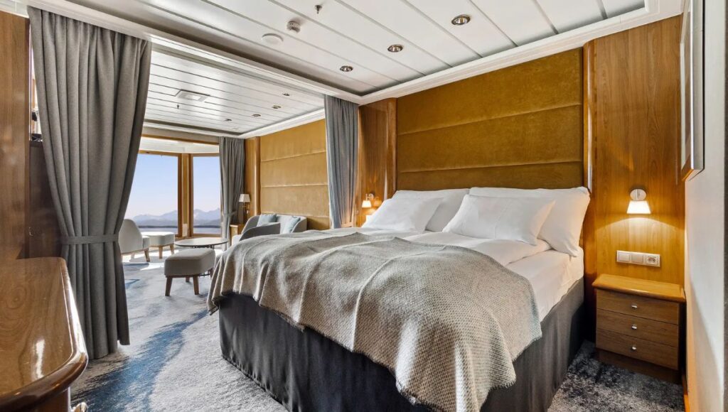 Spacious Hurtigruten cabin with double bed, separate seating area and warm wood furnishings.