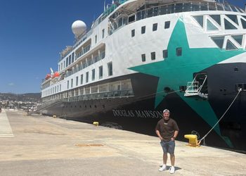Josh standing on the quayside beside AE Expeditions' Douglas Mawson, with the ship's green star livery on the bow behind him