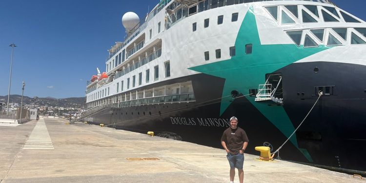 Josh standing on the quayside beside AE Expeditions' Douglas Mawson, with the ship's green star livery on the bow behind him