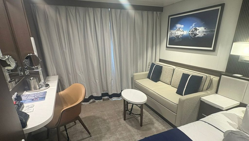 Seating area and desk in a Douglas Mawson balcony stateroom, with floor to ceiling curtains across the balcony door