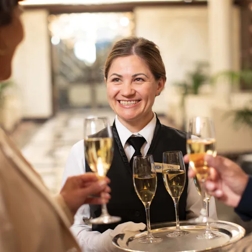 Regent crew member welcoming guests aboard with a glass of Champagne