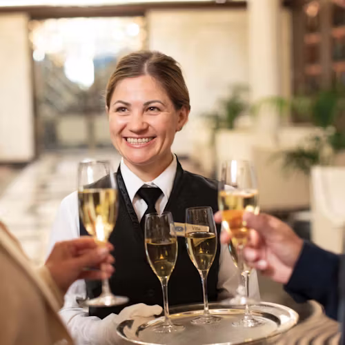 Regent crew member welcoming guests aboard with a glass of Champagne