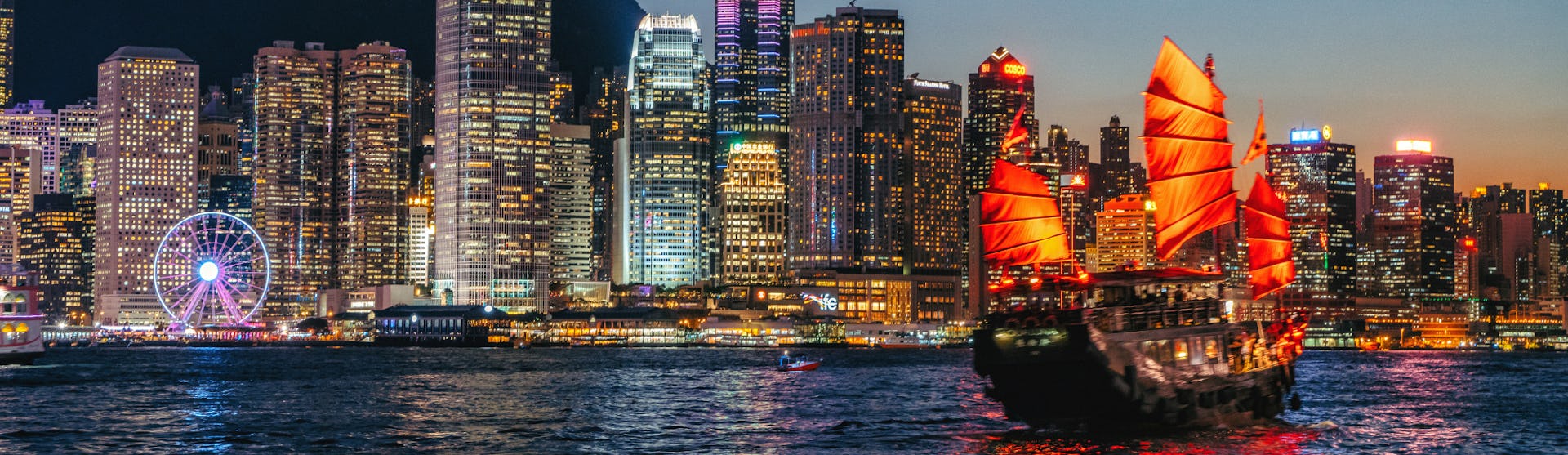 Traditional sail boat cruising in front of the skyline of Hong Kong