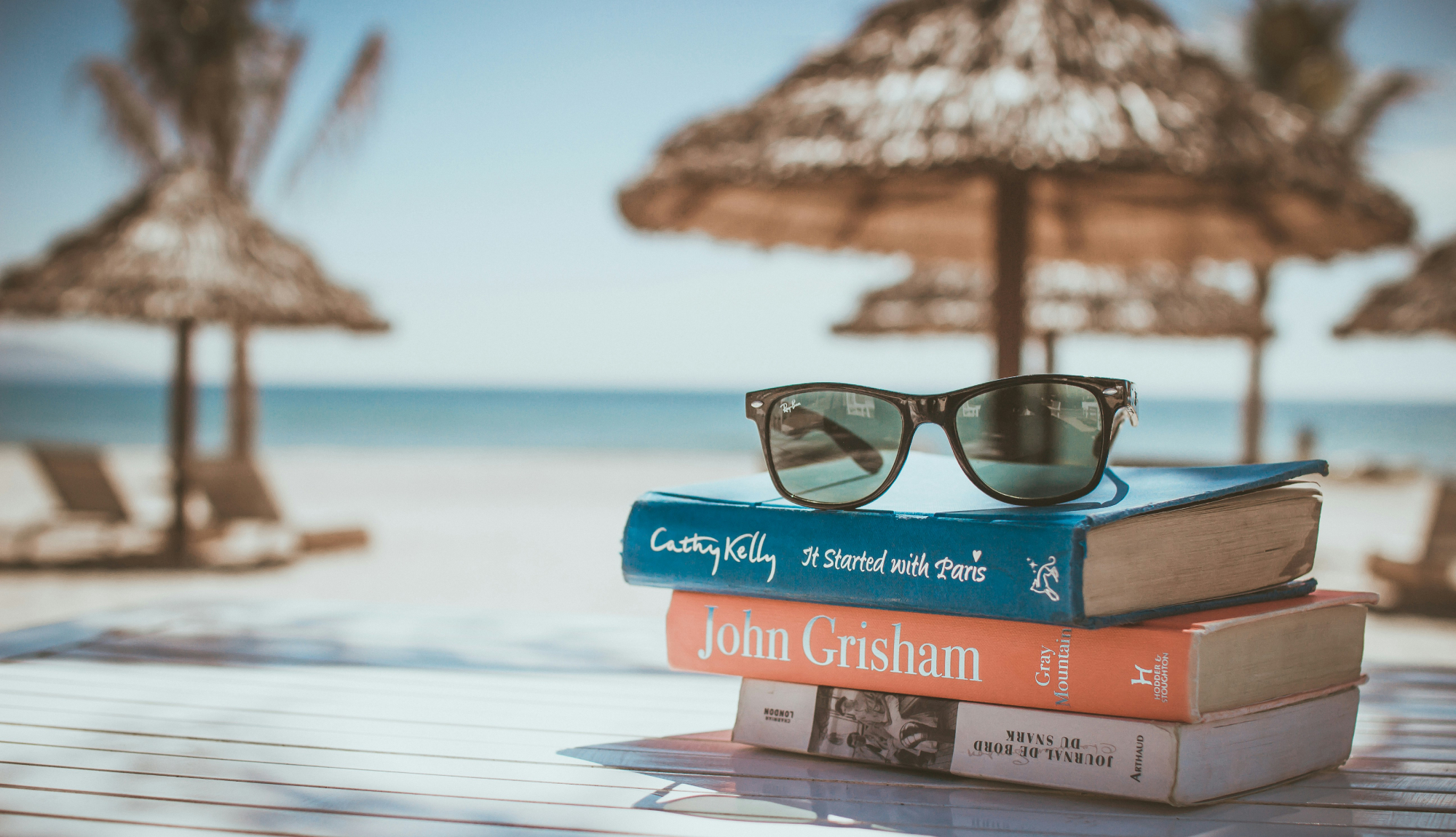 Sunglasses on top of a 3 books on a beach