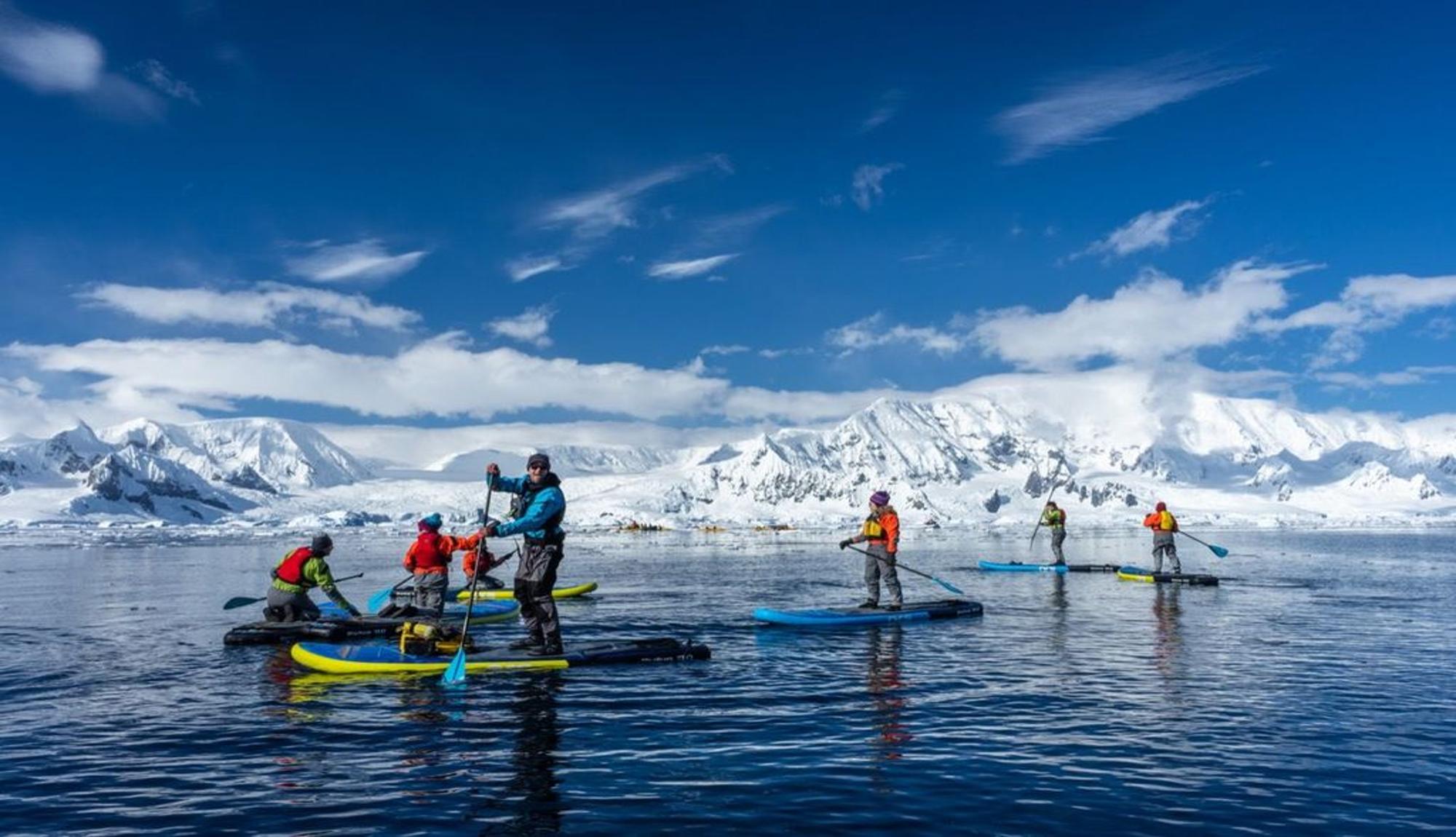 Paddleboarding group on an excursion in Antarctica with mountain views