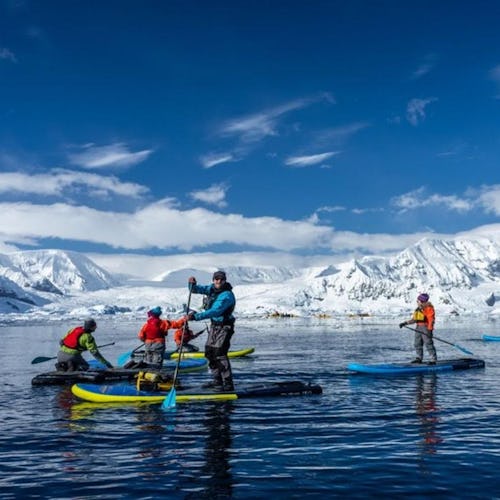 Paddleboarding group on an excursion in Antarctica with mountain views