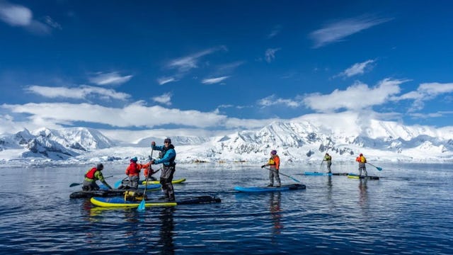 Paddleboarding group on an excursion in Antarctica with mountain views