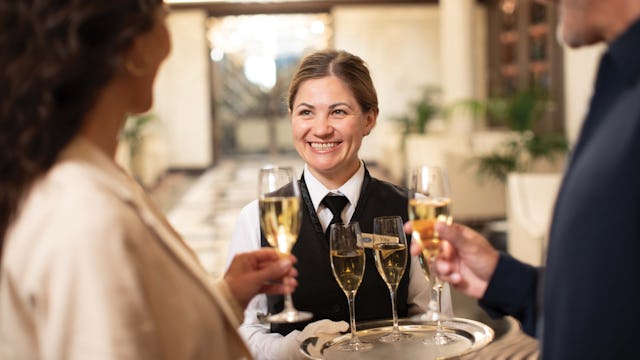Regent crew member welcoming guests aboard with a glass of Champagne